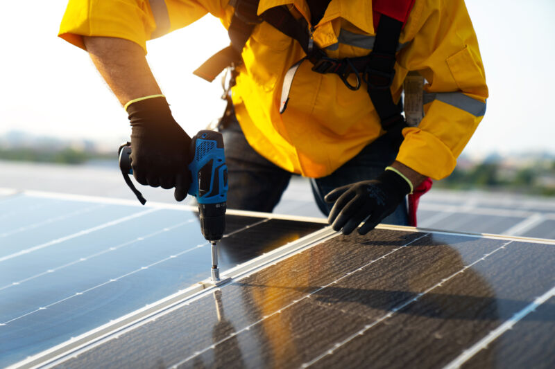 Técnico masculino con traje amarillo instalando paneles solares azules fotovoltaicos con tornillo.  hombre electricista panel sol recursos sostenibles fuente de energía renovable alternativa innovación